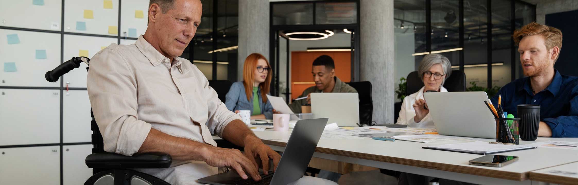 Team of office workers sat around large desk, one person sitting in a wheelchair